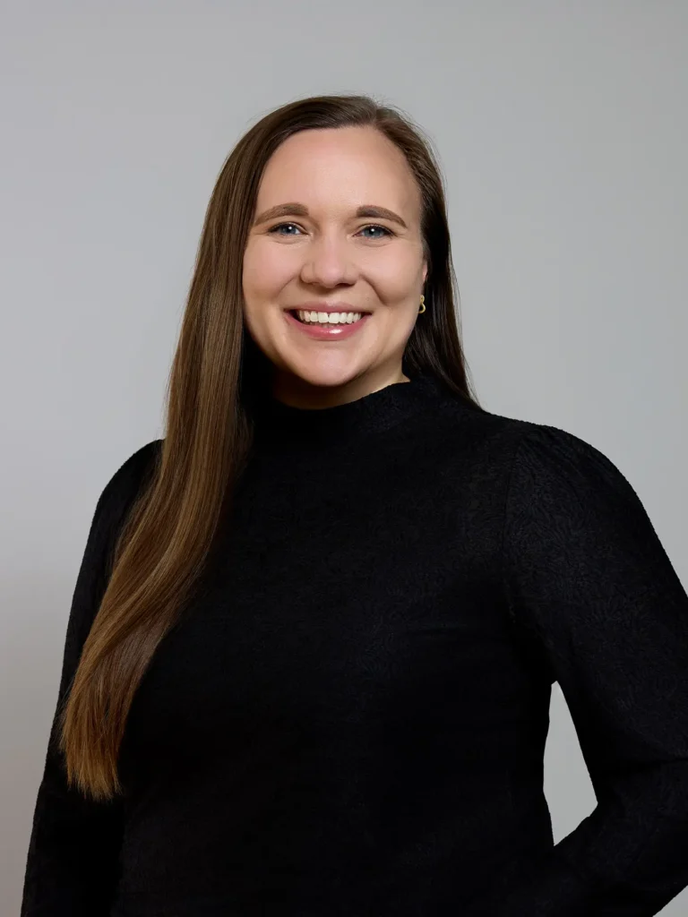 Porträt einer lächelnden Frau mit langen braunen Haaren und schwarzem Oberteil vor grauem Hintergrund, Reisebüro Hamburg